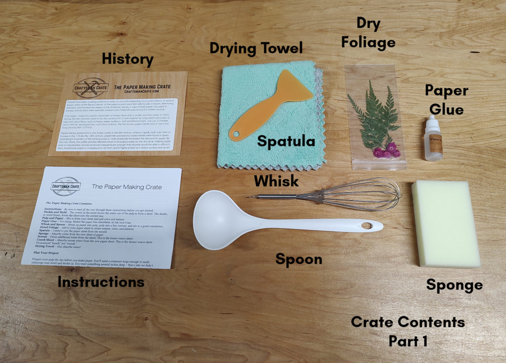 A photo of the history card, instructions, drying towel, spatula, dry foliage, paper glue, sponge, spoon, and whisk on light-colored wood.
