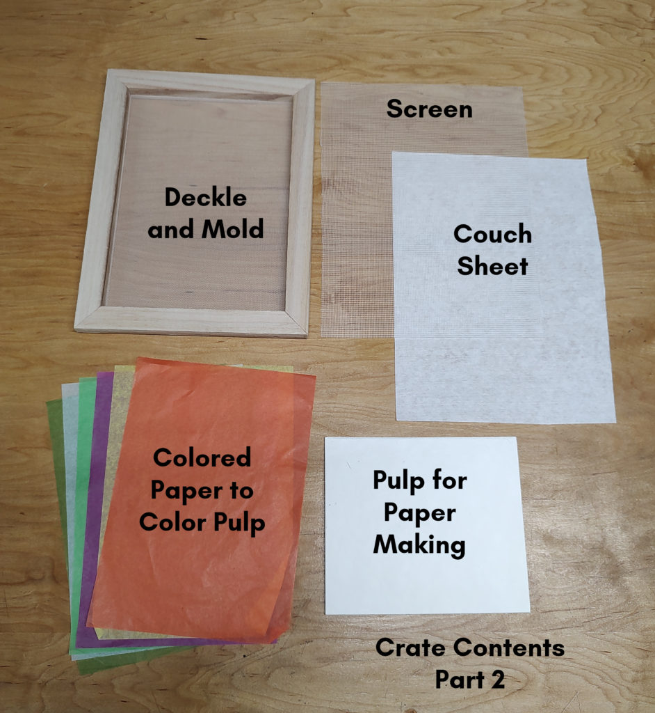 A photo of the deckle and mold, screen, couch sheet, colored paper, and pulp for paper making on light-colored wood.