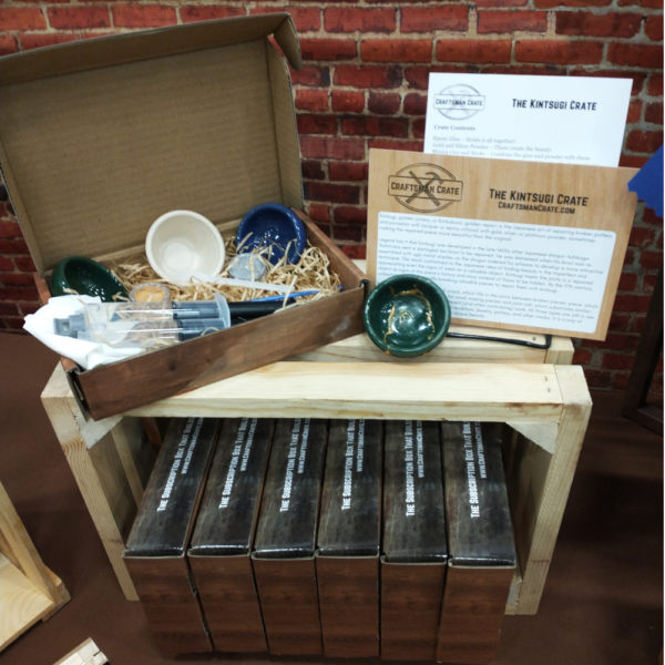Kintsugi Crate sitting on wooden box with green ceramic bowl repaired with gold and unopened kits beneath it with a brick background