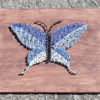 A string art butterfly in shades of blue with a black body on a stained board.