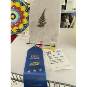 Handmade paper with a fern embedded displayed at the State Fair with a blue first place ribbon
