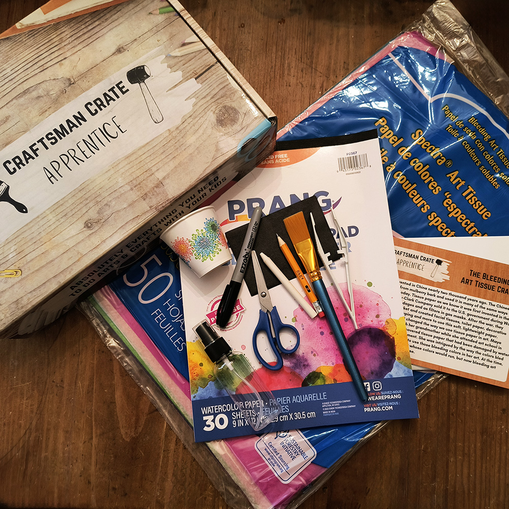 Bleeding Art Tissue Kit From Above 1000x1000 Photo of Apprentice Bleeding Art Tissue Crate from above showing a large package of bleeding art tissue, a watercolor paper pad, scissors, a spray bottle, a brush, a white crayon, a cup, a pencil, a permanent marker, instructions, and a splash card.