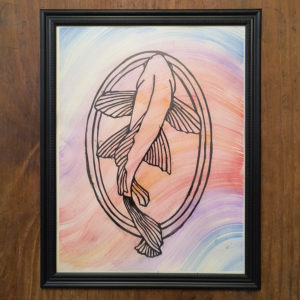 A Koi Fish cut into black paper in a Japanese style over a watercolor wash background in a black frame on a wooden table.